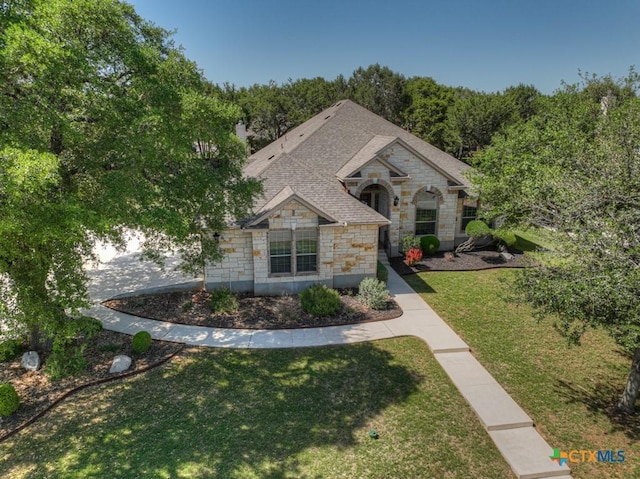 french country style house featuring a shingled roof, stone siding, and a front lawn