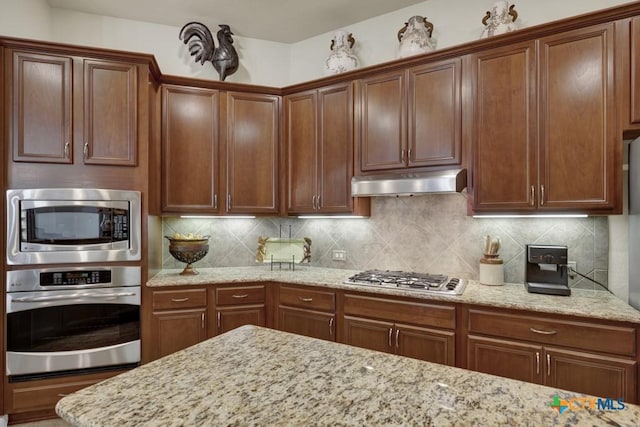 kitchen featuring appliances with stainless steel finishes, decorative backsplash, light stone countertops, and under cabinet range hood