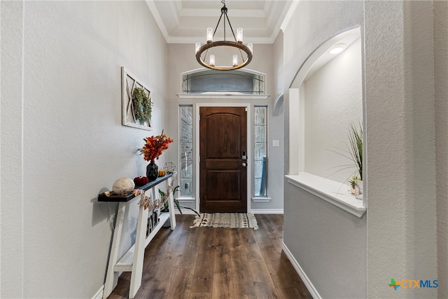 foyer entrance with a tray ceiling, an inviting chandelier, dark wood-type flooring, and ornamental molding