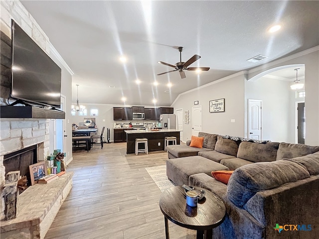 living room with a stone fireplace, light hardwood / wood-style floors, lofted ceiling, ornamental molding, and ceiling fan