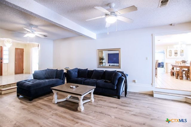 living room with ceiling fan, beamed ceiling, light hardwood / wood-style floors, and a textured ceiling