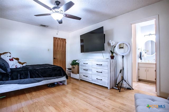 bedroom with a textured ceiling, light wood-type flooring, ensuite bath, and ceiling fan