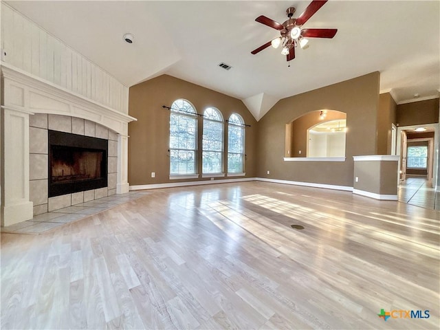 unfurnished living room with ceiling fan, vaulted ceiling, a tile fireplace, and light wood-type flooring