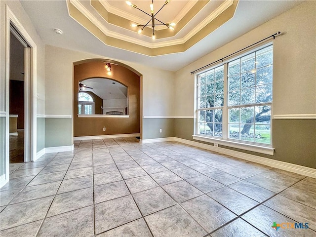 tiled empty room featuring ceiling fan with notable chandelier, ornamental molding, and a raised ceiling