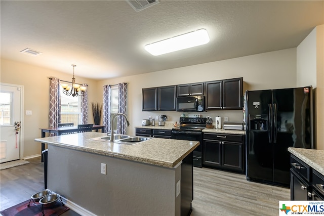 kitchen with a center island with sink, sink, black appliances, light hardwood / wood-style flooring, and pendant lighting