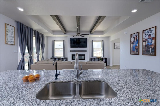 kitchen with a large fireplace, open floor plan, beamed ceiling, light stone countertops, and a sink