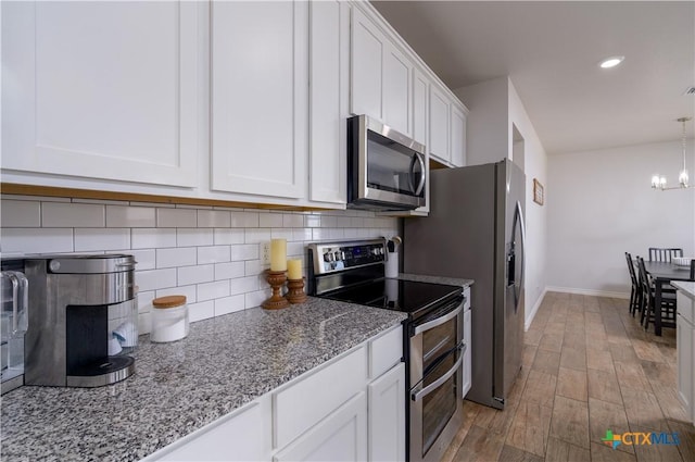 kitchen with hanging light fixtures, light stone countertops, stainless steel appliances, white cabinetry, and backsplash