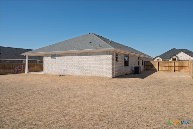 back of house featuring central AC, brick siding, and a fenced backyard