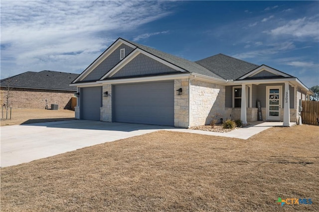 view of front of property with a shingled roof, concrete driveway, stone siding, an attached garage, and a front lawn