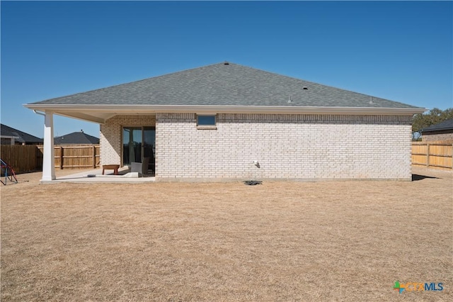 rear view of house featuring a patio area, a shingled roof, fence, and brick siding