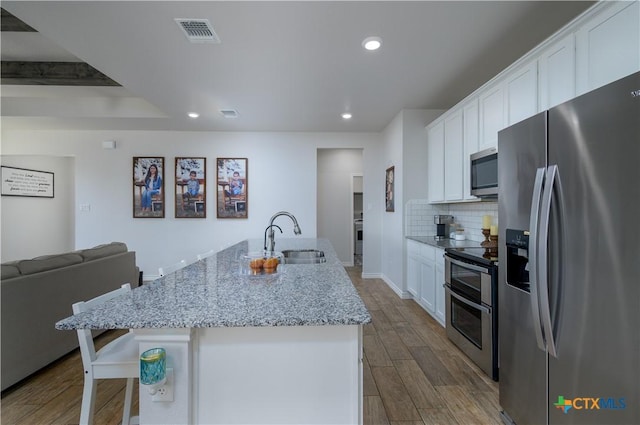 kitchen with a center island with sink, visible vents, appliances with stainless steel finishes, white cabinetry, and a sink