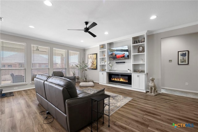 living area with ornamental molding, a glass covered fireplace, dark wood-style flooring, and baseboards