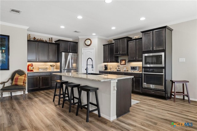 kitchen with light wood finished floors, a kitchen island with sink, appliances with stainless steel finishes, and a sink