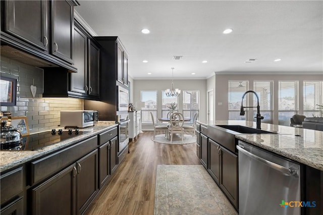 kitchen featuring wood finished floors, a sink, appliances with stainless steel finishes, light stone countertops, and crown molding