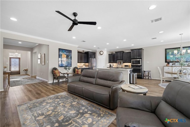 living area featuring light wood finished floors, baseboards, visible vents, and crown molding