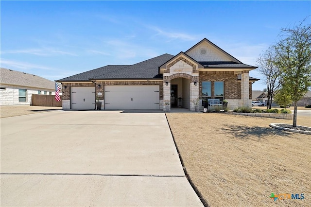 view of front of home featuring a garage, concrete driveway, stone siding, roof with shingles, and brick siding