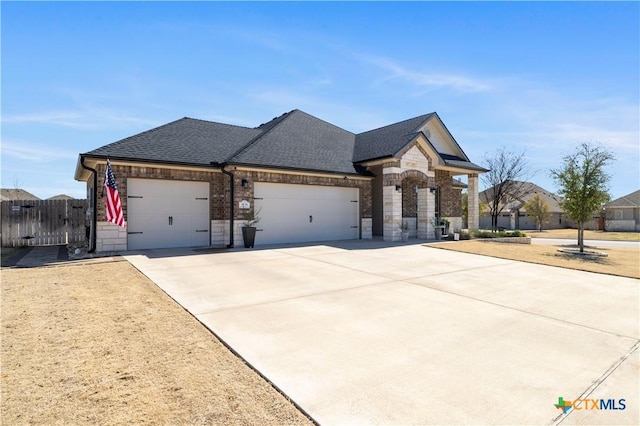 french provincial home with roof with shingles, concrete driveway, fence, a garage, and stone siding