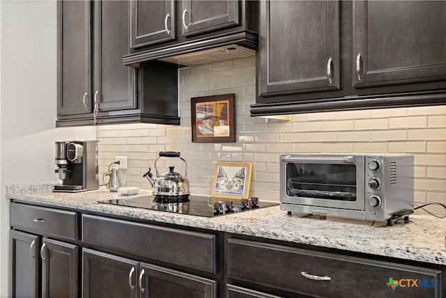 kitchen with a toaster, custom exhaust hood, tasteful backsplash, dark brown cabinetry, and light stone countertops