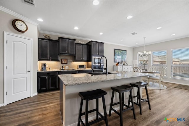 kitchen featuring tasteful backsplash, visible vents, a breakfast bar area, wood finished floors, and a sink