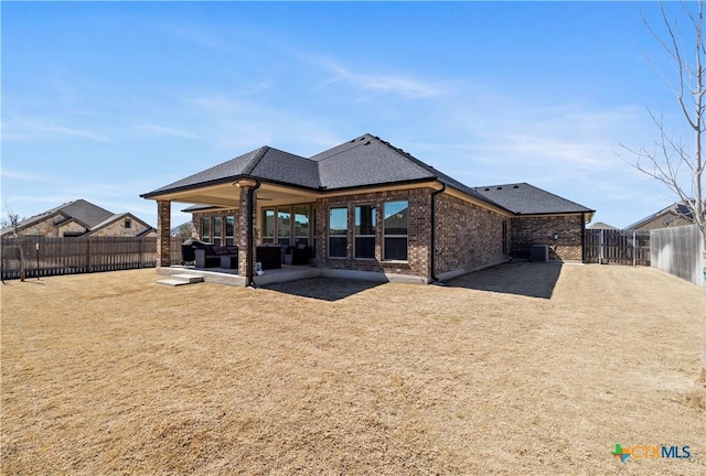 rear view of house featuring a shingled roof, brick siding, a patio, and a fenced backyard