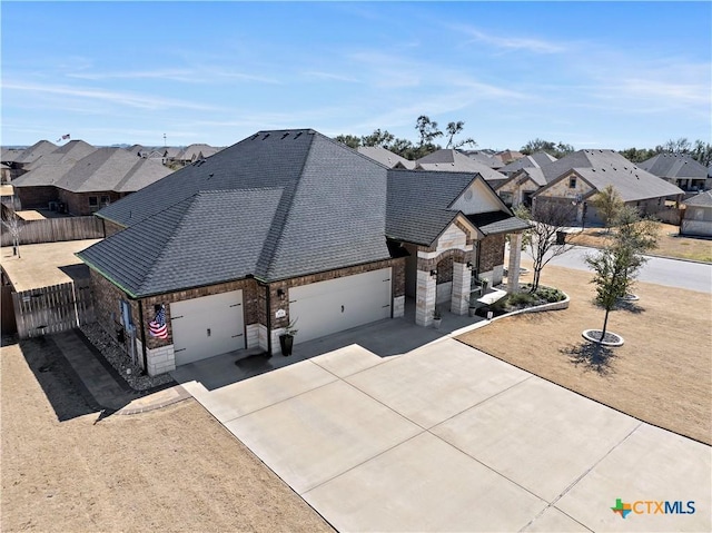 view of front facade with concrete driveway, an attached garage, fence, a residential view, and stone siding