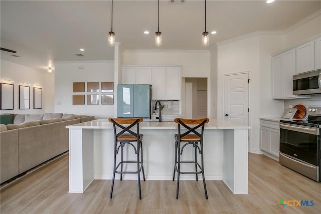 kitchen with appliances with stainless steel finishes, decorative light fixtures, white cabinetry, and a kitchen island with sink