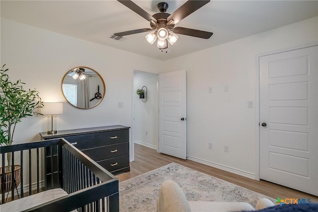 bedroom featuring ceiling fan, a crib, and hardwood / wood-style flooring