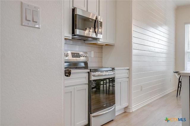 kitchen featuring tasteful backsplash, white cabinetry, light wood-type flooring, and appliances with stainless steel finishes