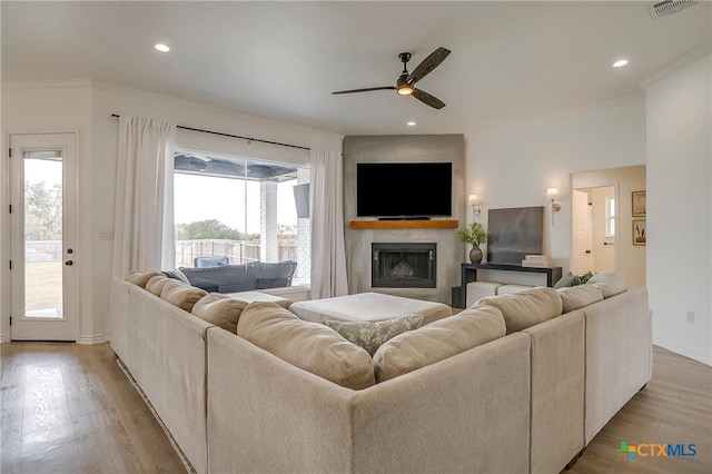 living room with a large fireplace, ceiling fan, light hardwood / wood-style floors, and a healthy amount of sunlight