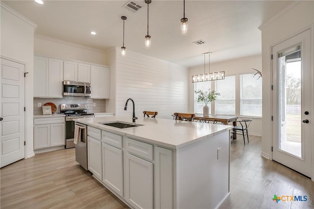 kitchen with a center island with sink, sink, appliances with stainless steel finishes, decorative light fixtures, and white cabinetry