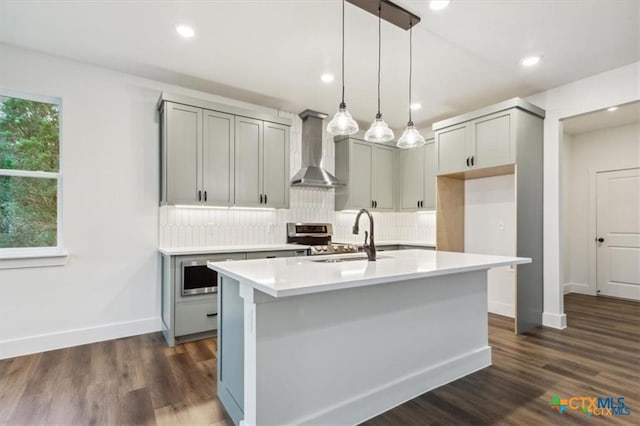 kitchen with sink, wall chimney exhaust hood, an island with sink, pendant lighting, and gray cabinets