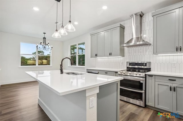 kitchen featuring a center island with sink, sink, wall chimney exhaust hood, gray cabinets, and stainless steel range