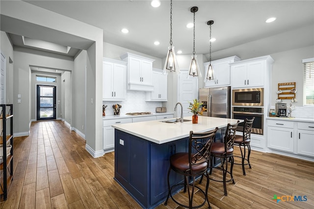 kitchen with a sink, light countertops, wood-type flooring, appliances with stainless steel finishes, and a kitchen breakfast bar