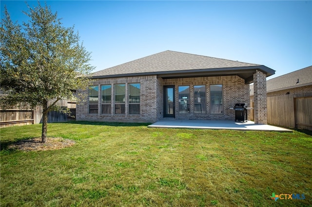 rear view of house featuring a patio, roof with shingles, a fenced backyard, a lawn, and brick siding