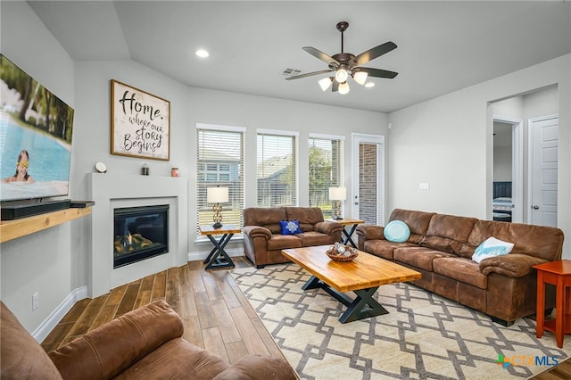 living room featuring light wood finished floors, visible vents, baseboards, ceiling fan, and a glass covered fireplace