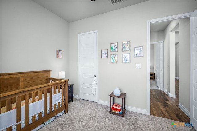 carpeted bedroom featuring baseboards, a crib, and visible vents