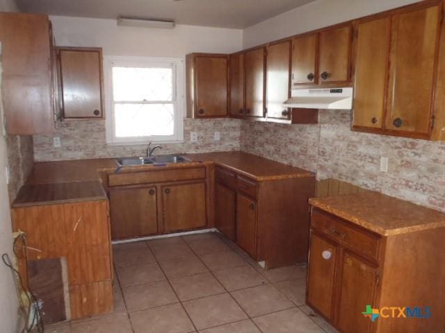 kitchen with brown cabinets, a sink, and under cabinet range hood