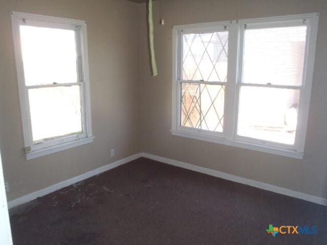 unfurnished room with dark colored carpet and baseboards