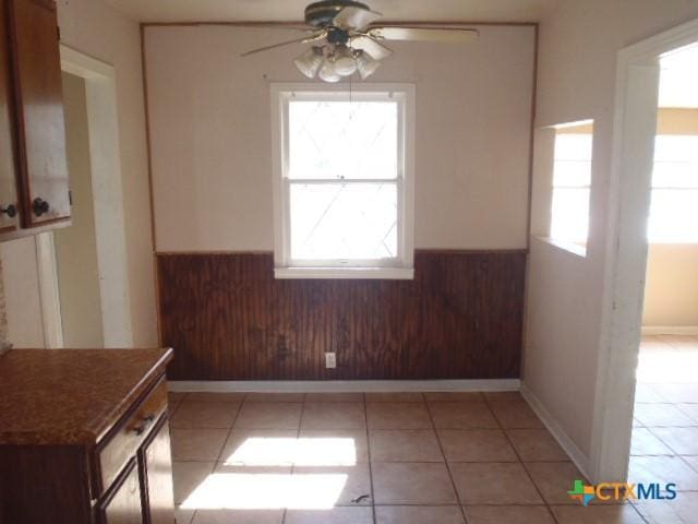 unfurnished dining area featuring a wainscoted wall, wooden walls, and light tile patterned flooring