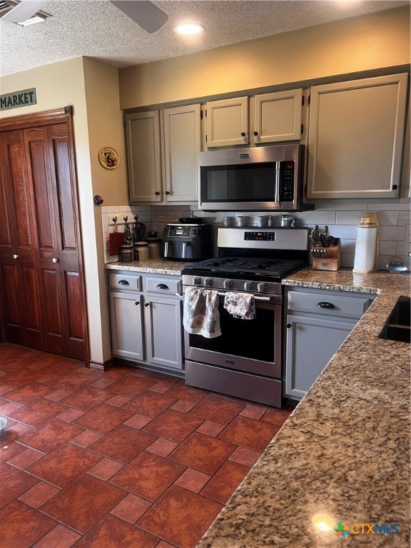 kitchen featuring decorative backsplash, a textured ceiling, gray cabinets, ceiling fan, and appliances with stainless steel finishes