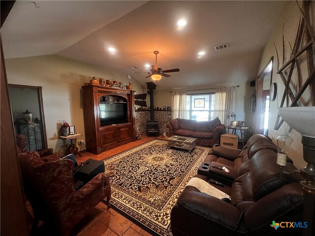 living room with ceiling fan, tile patterned floors, a wood stove, and vaulted ceiling