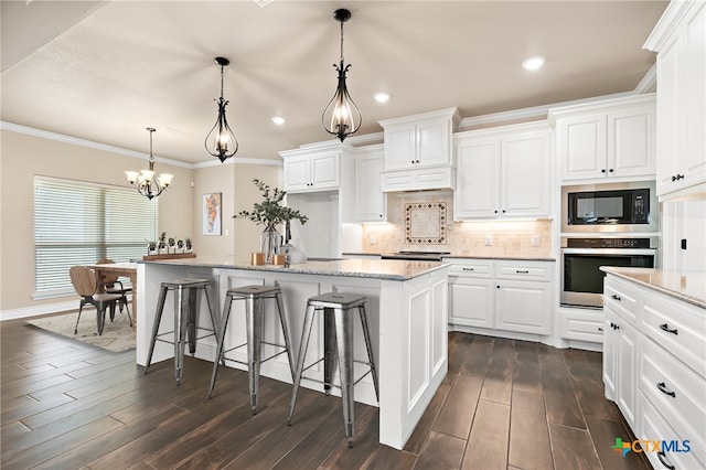 kitchen featuring decorative light fixtures, black microwave, white cabinets, oven, and a kitchen island with sink