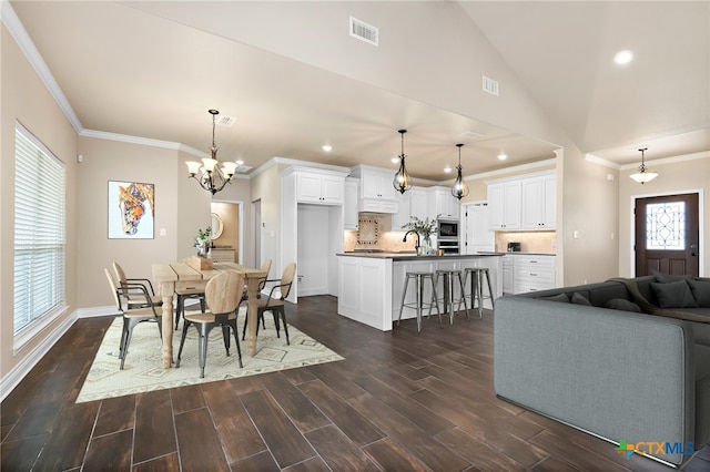 dining area featuring lofted ceiling, sink, dark wood-type flooring, ornamental molding, and a chandelier