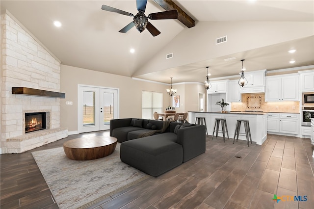 living room featuring ceiling fan with notable chandelier, a fireplace, high vaulted ceiling, beam ceiling, and french doors