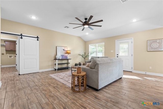 living room featuring a barn door, ceiling fan, light hardwood / wood-style flooring, and vaulted ceiling