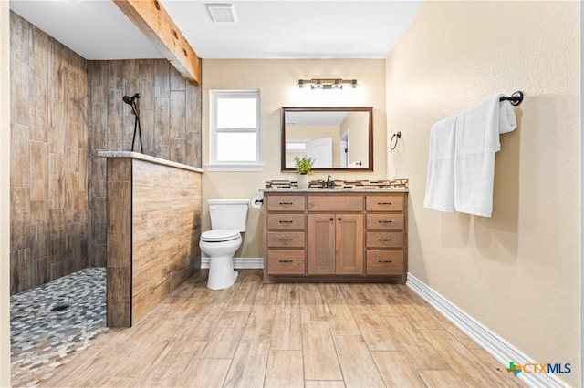 bathroom with hardwood / wood-style floors, vanity, toilet, and tiled shower