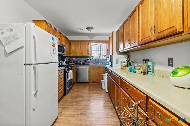 kitchen featuring appliances with stainless steel finishes, brown cabinetry, a sink, and light wood-style flooring