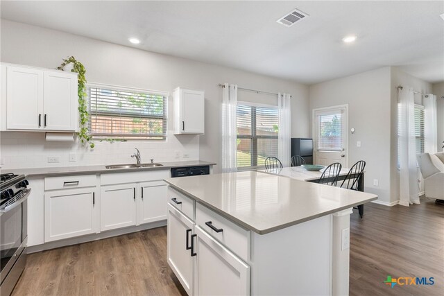 kitchen featuring stainless steel range with gas cooktop, visible vents, decorative backsplash, a sink, and wood finished floors