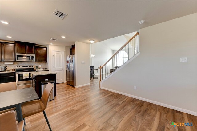 kitchen featuring light stone counters, backsplash, light wood-type flooring, appliances with stainless steel finishes, and dark brown cabinets