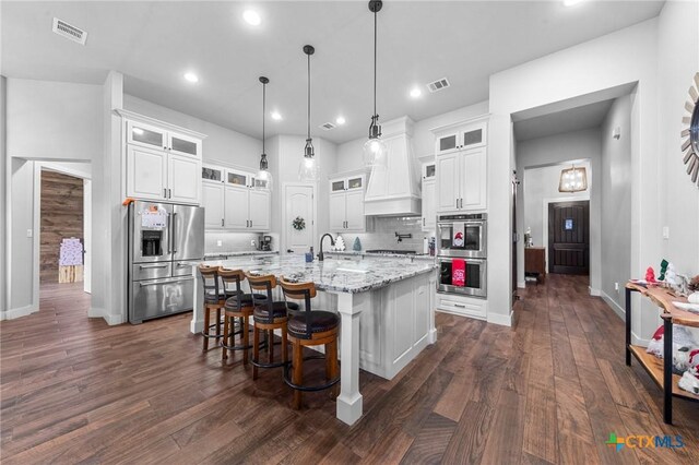 kitchen featuring light stone countertops, stainless steel appliances, backsplash, an island with sink, and white cabinets